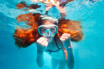 Beautiful underwater portrait of the smiling little girl with long hairs wearing scuba mask show hands gesture