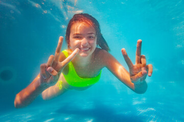 Happy smiling teen girl with v victory hands expression and big smile swim underwater in the pool