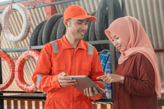 male mechanic in a wearpack uniform and a female customer using a digital tablet to view the catalog at a spare part workshop