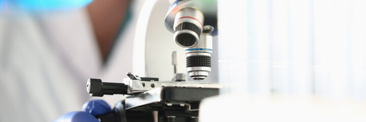 Close up of male researcher in sterile gloves looking at biological samples under microscope