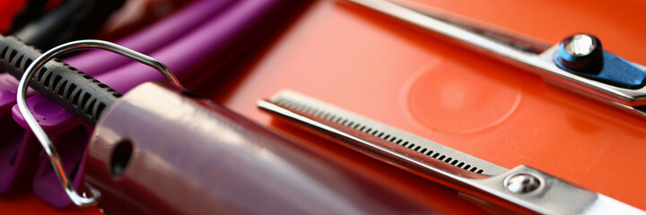 Close up of professional hairdressing scissors, hair clipper and hairgrips on red surface