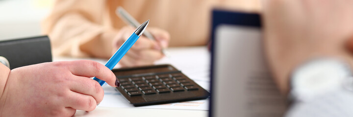 Close up of young man holding blue pen while sitting at the table with calculator and working with...