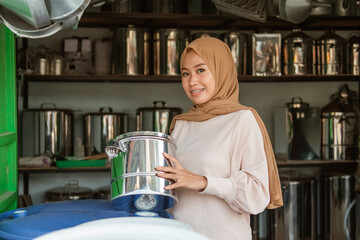 hijab female seller smiling when look at camera while holding the pan in the household appliances store