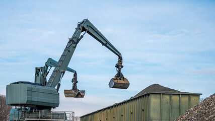 Big excavator working by handling pebbles from the pile of stones to container. Working machine in...