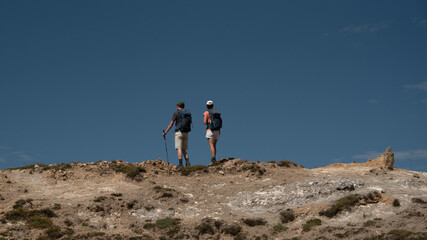 a young woman and a young man standing, side by side, looking at the horizon at the top of a mountain