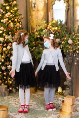 little sisters are surprised. red-haired girls in medical masks stand near the Christmas tree. sad