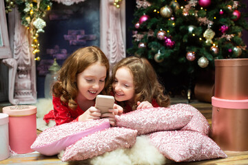two red-haired sisters near the New Year trees, looking at the phone. Christmas, gadgets, online
