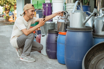 asian male seller squat using phone camera when taking photo a kettles in front of the household appliances store