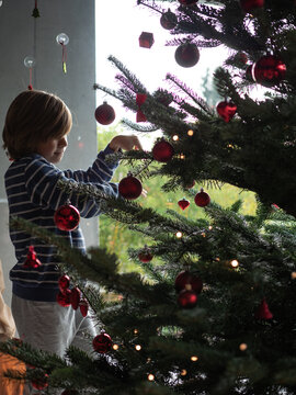 Winter holidays, charity and people concept. Happy boy decorating christmas tree at home.