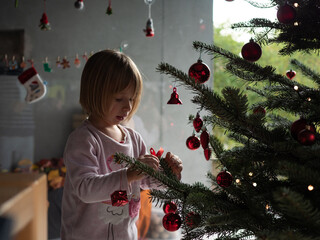 Winter holidays, charity and people concept. Happy little girl decorating christmas tree at home.