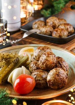 Holiday homemade meat cutlets with pickles in plate on wooden table served with glasses, bottle of wine, candles, fir branches, festive decoration, garland. Christmas and New Year food, bokeh, lights