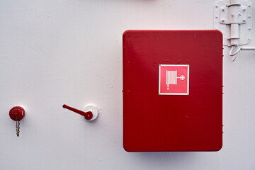 A red fire shield on a white wall on a ship.