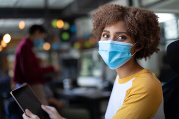 Portrait of mixed race woman wearing face mask using tablet in casual office