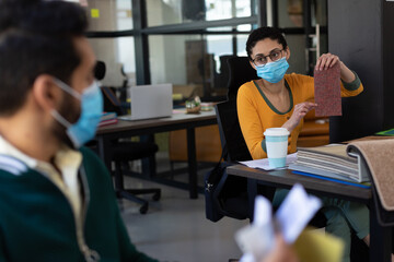 Mixed race woman wearing face mask discussing fabric sample in office