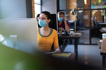 Diverse colleagues wearing face masks working with computers at office desks