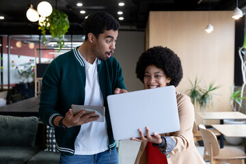 Happy diverse businessman and businesswoman using laptop and tablet in office