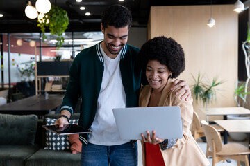 Happy diverse businessman and businesswoman using laptop and tablet in office