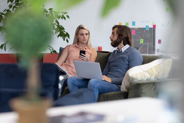 Caucasian businessman and businesswoman using laptop in creative office