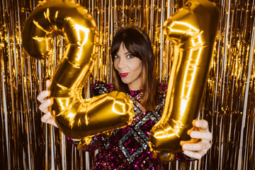 .Beautiful woman dressed for New Years Eve in a sparkling dress. Fun and festive attitude. Holding metallic balloons. Year 2021