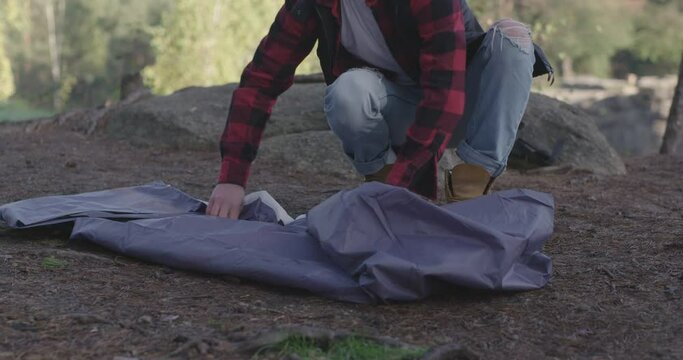 Tourist unfolds, unrolls tent to set it up, making camping place.
