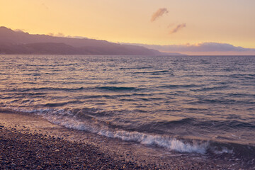 Obraz premium Waves on the pebble shore of the sea at sunset in Crete in Greece.