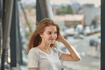 Fototapeta premium Happy young blonde woman with long hair smiles and looks away. Hair flying in the wind. Against the background of iron pipes.