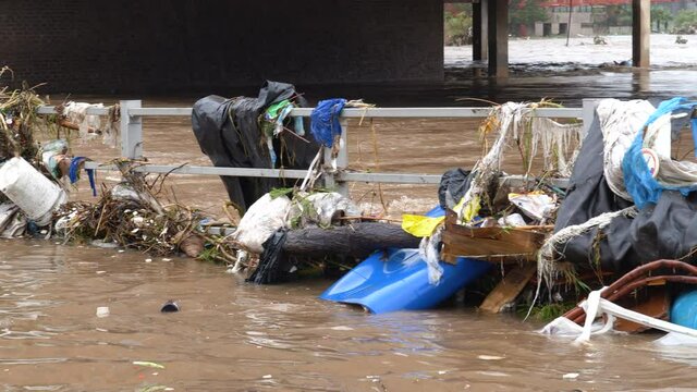 Close-up panning view of debris and plastic rubbish that wash up against road bridges in a city centre as a river comes down in flood from heavy rains due to climate change