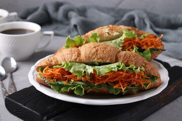 Two vegetarian croissants-sandwiches with lettuce, carrots, cucumbers and two cups of coffee on a light grey concrete background. Breakfast or lunch concept
