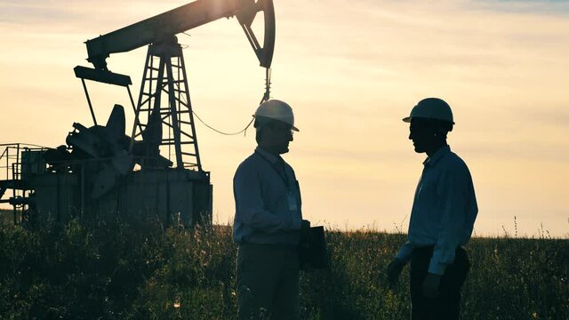 Two oil workers shaking hands with oil pumpjack operating in background