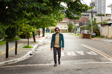 Homem elegante, usando &oacute;culos de sol e blazer, caminhando na rua.