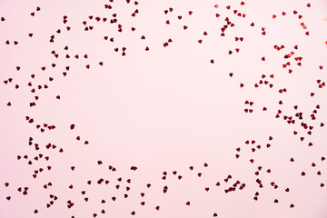 Frame border of red heart shaped confetti on pink background. Flat lay, top view, copy space. Happy Valentines Day, Mothers Day, birthday concept.