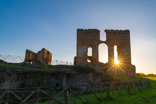 Villa dei Quintili, Rome, the thermal baths, a suggestive panoramic image of the brick building of the caldarium at sunset with the sun rising from the ruins and the blue sky in Via Appia.
