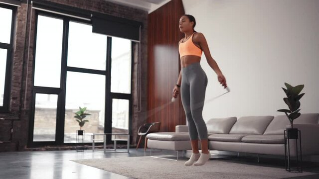 Athletic African American beautiful woman jumping rope as part of her fitness workout in a cozy home environment.
