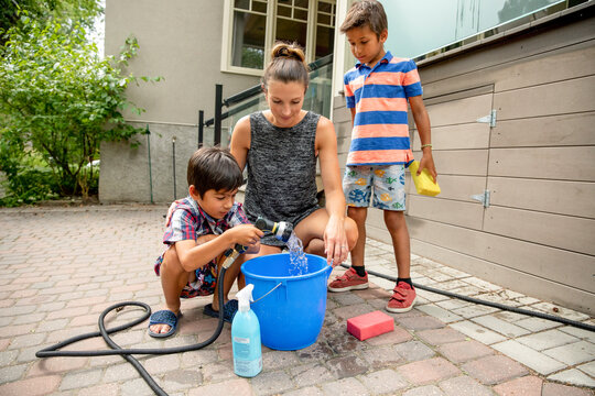 Mother and sons filling up pail with water in backyard