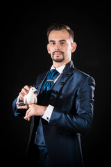 Handsome male magician with a beard and mustache with a stern face in a blue tailcoat holding a dove on a black background