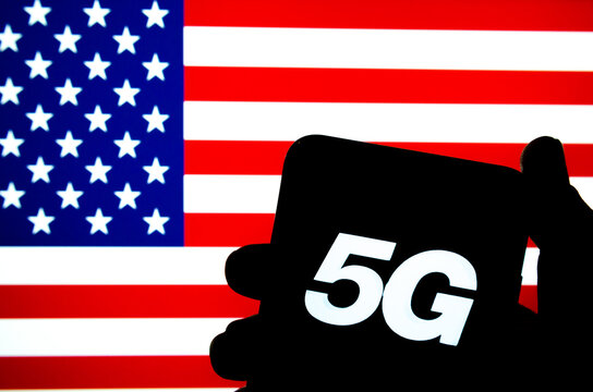 5G letters on a silhouette of a smartphone hold in hand with the flag of the United States on a blurred background screen. Authentic photo, not a montage or illustration. No alteration in post.