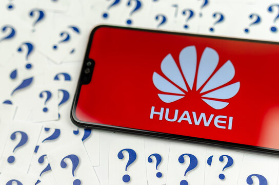 HUAWEI logo on the HUAWEI smartphone and a lot of paper question marks around. The conceptual photo about future of the tech giant in the US.