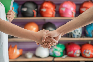 Fototapeta na wymiar helmet seller shakes hands with customer against helmet display rack background