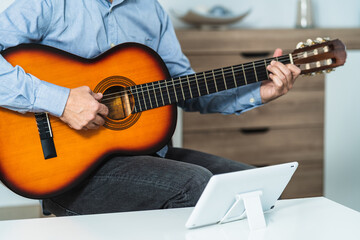 Obraz premium Caucasian male receiving online Spanish guitar lessons with the tablet