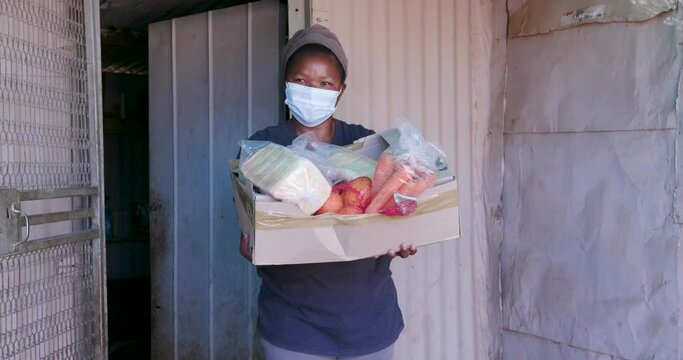 Black African woman standing holding a food parcel donated to her while in lockdown for Covid-19 Coronavirus pandemic in South Africa
