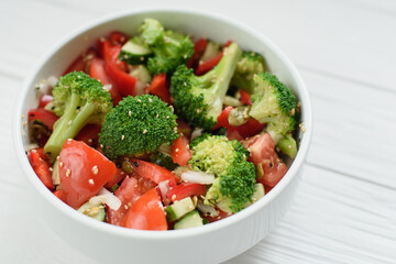 Vegetable salad. bowl of salad with fresh vegetables and greens, cucumber, tomatoes, red pepper, broccoli cabbage. and olive oil on white background. Top view. Healthy food.