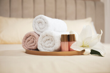 Rolled clean towels, flower and shampoo bottles on bed