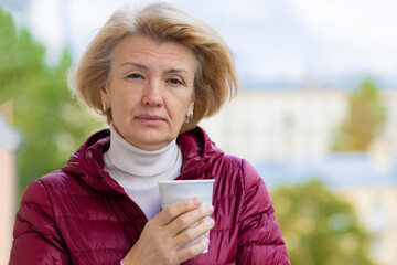 elegant senior adult woman outdoors with coffee, in the wind, with developing hair