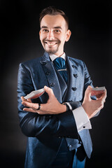 A magician in a blue tailcoat with a wide smile holds cards in his hands