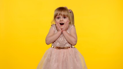 Portrait of happy amazed astonished young kid girl in shiny dress isolated on yellow copy space background. Impressed child. Perfect surprise. Exciting news. Wow reaction.