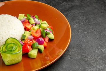 Close up view of homemade rice dish and salad with tomato and cucumber on dark table