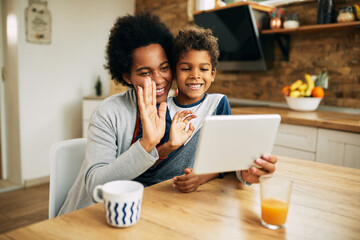 Happy African American mother and son waving during video call at home.