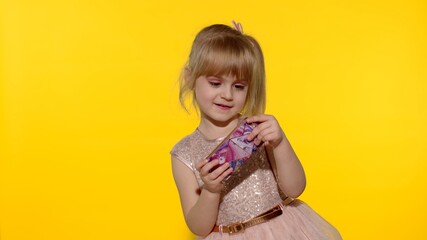 Little girl using smartphone. Portrait of child texting on smartphone. Kid enthusiastically playing games on mobile phone isolated on yellow background in studio. Technology for children