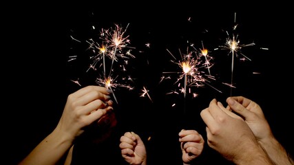 Close-up of hands or palms holding and waving burning sparklers in front of black dark background. Sparkling lights at birthday party, wedding, New Year, Christmas Eve, Xmas. 6k downscale. Bengal fire