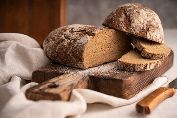Sliced loaf of black bread on the old rustic wooden cutting board. Selective soft focus.